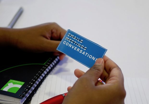 Photo of someone holding a Defra sticker that says "Email meetings conversations" (the words "email" and "meetings" are crossed out).