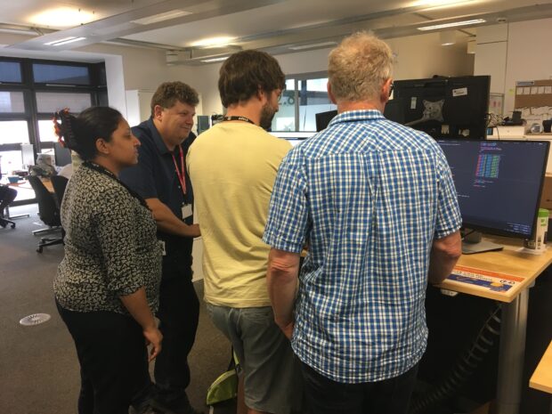 People stand around a desk looking at a display screen