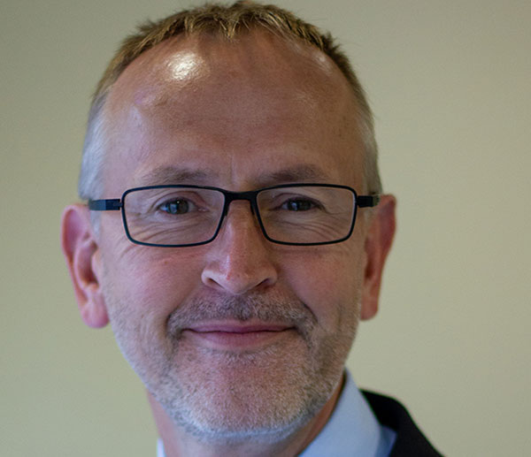 man with short hair, glasses and a beard, wearing a white shirt.