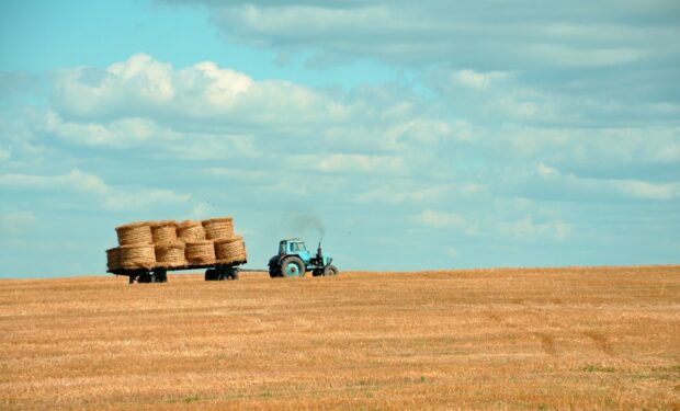 A picture of a green tractor pulling a trailer of hay bails across a field under a blue sky