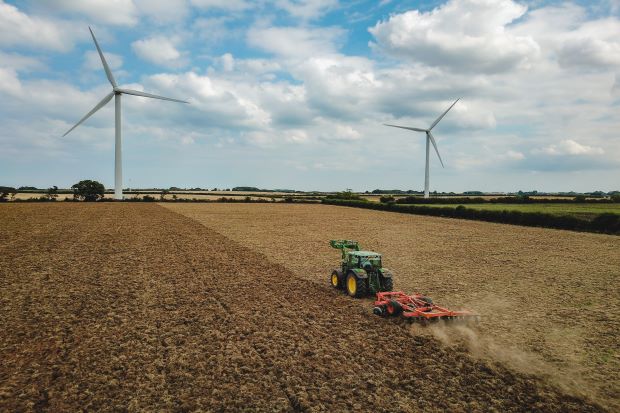 A tractor ploughing the field with wind turbines in the background