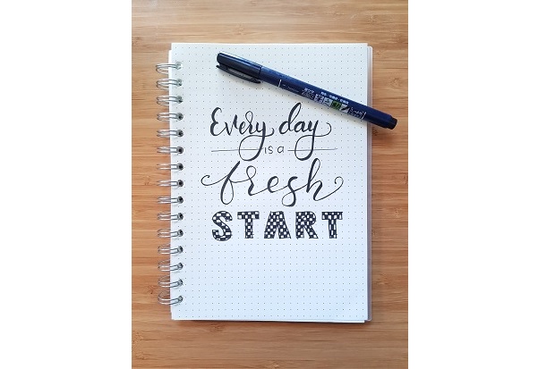 A ring-bound writing pad, bearing the words 'every day is a fresh start' on the cover, along with a pen.