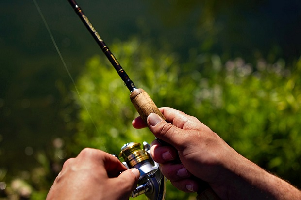 A pair of hands, holding a fishing rod and reel.