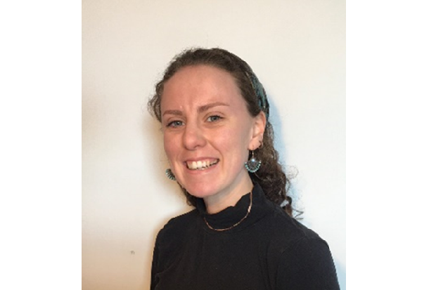 Side on picture of a lady, with curly shoulder length hair, wearing earrings, a necklace and a black sweater.