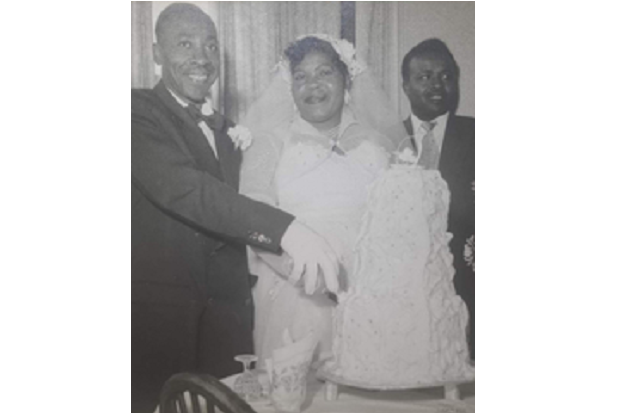 A black and white picture of a married couple cutting a wedding cake.