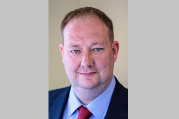 A man with short hair wearing a dark suit and a red tie