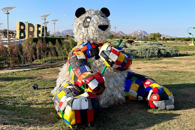 A giant model of a panda, made from plastic bottles, and with multi coloured patches on its arms and legs.