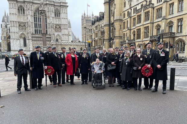 A man in military uniform, in the street, joined by others in a parade-style format.