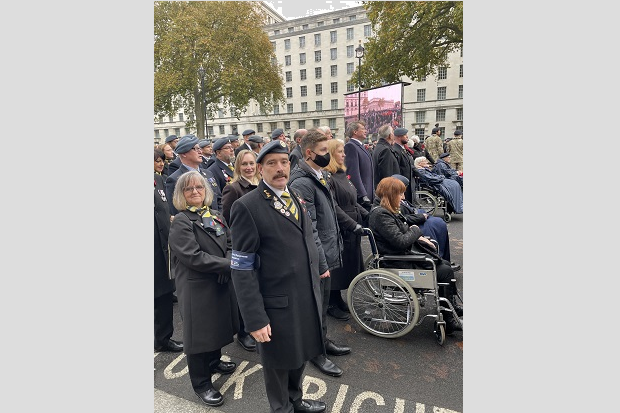 A man in military uniform, in the street, joined by others in a parade-style format.