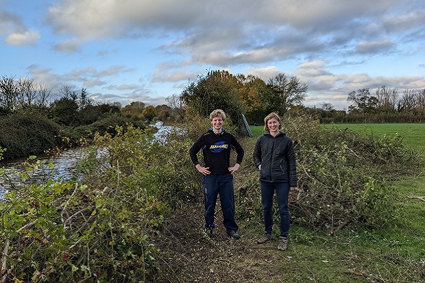 Tom by the canal with a pile of cut branches next to him