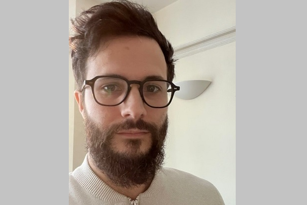 A man with short dark hair, glasses and beard.