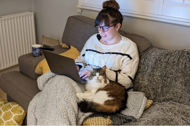 Melissa Massey, sitting on a sofa, working on her laptop computer with a her cat sat next to her.