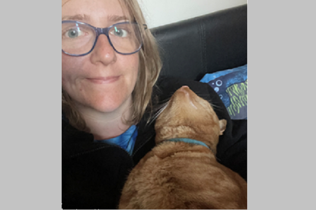 A lady with glasses and long blond hair, holding a ginger cat.