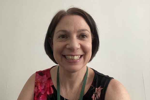 Head and shoulders view of a lady with dark, bobbed hair, and wearing a flowered dress and green lanyard.