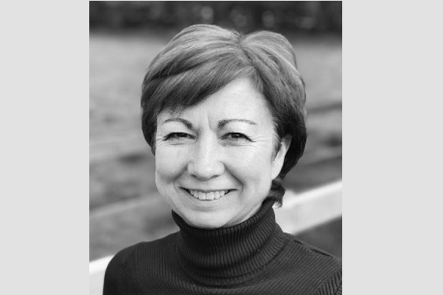 A black and white picture of a white lady, smiling, with short dark hair, and wearing a black polo neck sweater.