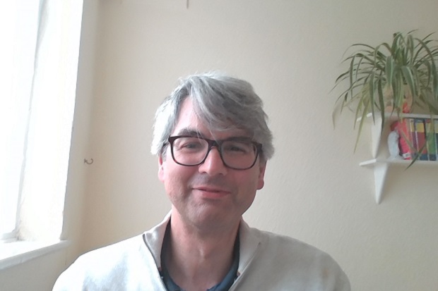 A man with grey hair and glasses, wearing a white shirt