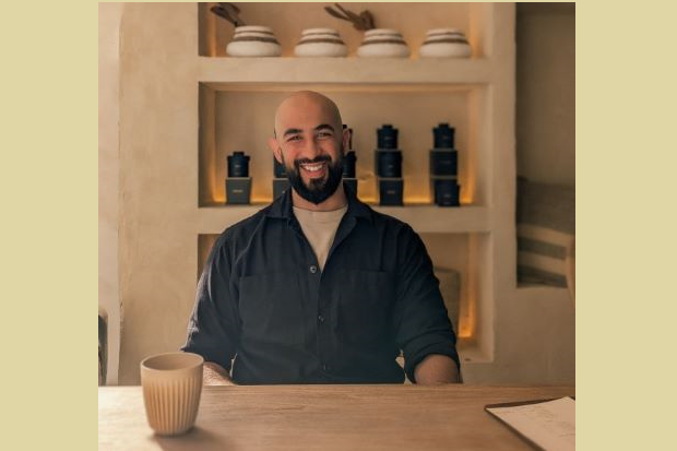 A man with a beard and wearing a blue shirt, sitting at a table.