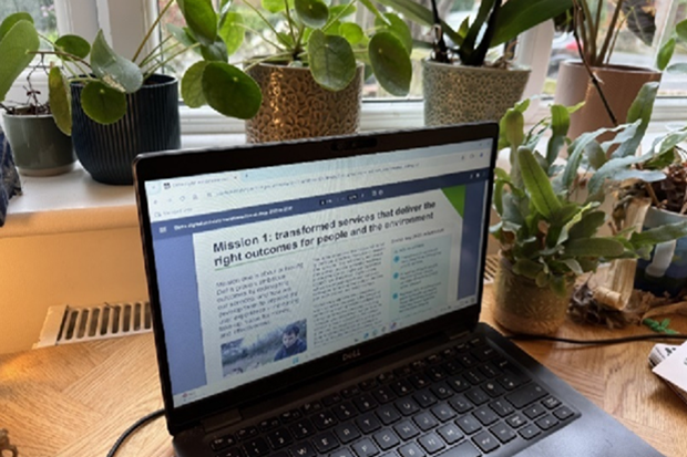 A laptop screen on a table, with potted plants in the background