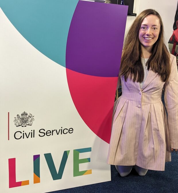 A woman with long brown hair standing next to a Civil Service Live banner