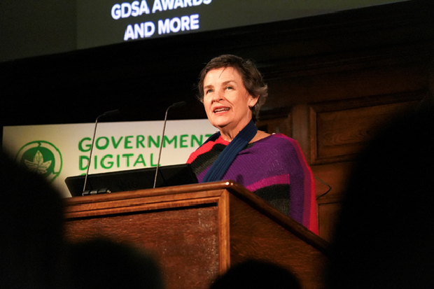 Photograph of a person standing behind a wooden podium with microphones, delivering a speech at an event. A sign behind the podium reads "Government Digital," indicating a conference or awards ceremony related to digital government services.