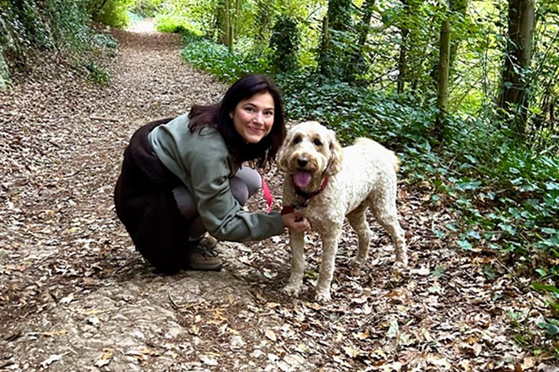 A lady with long dark hair, kneeling and holding a brown dog.